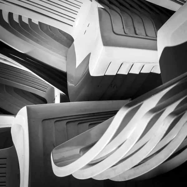 Monochromatic digital photograph of stacks of plastic chairs, emphasizing their abstract forms.